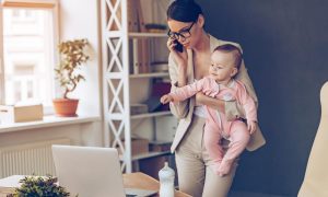 woman talking on the phone and looking at computer screen while holding a baby