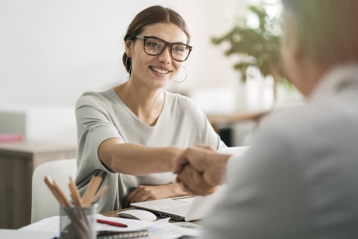 Female manager smiling and shaking her employee's hand as she concludes their stay interview.